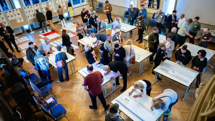 Mitglieder des Thüringer Bürgerrates "Frieden und Diplomatie" arbeiten in einem Saal stehend an Tischen und Stellwänden